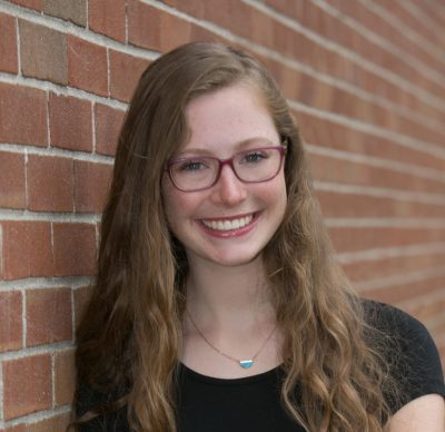 Headshot of woman with glasses in front of brick wall